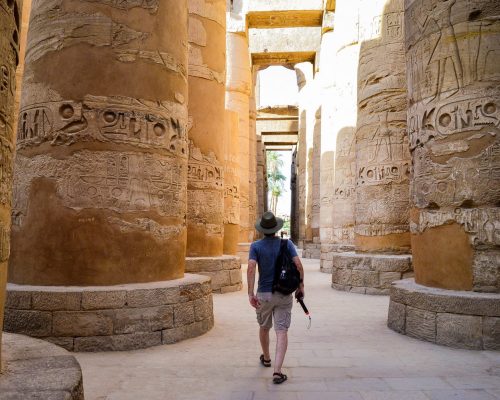 A low angle shot of a male walking between columns in  Karnak Temple in Egypt