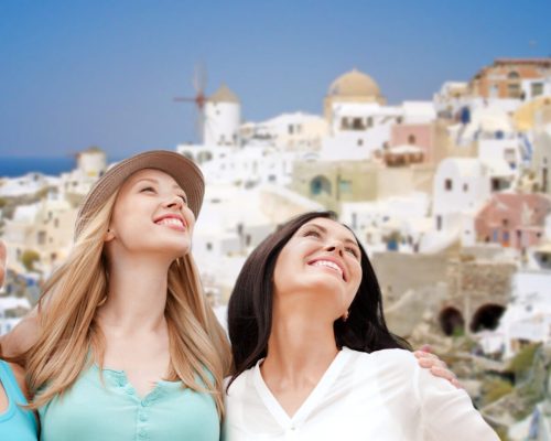 travel, tourism and summer vacation concept - group of happy smiling women or friends over oia town on santorini island background