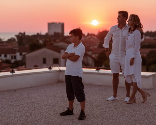 The happy family enjoys and spends time together on the roof of the house while watching the sunset on the open sea together. High-quality photo