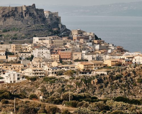 A vertical shot of buildings on the hill near the sea under a blue sky at daytime