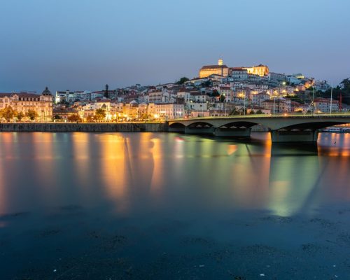 A bridge on the sea surrounded by Coimbra with the lights reflecting on the water in Portugal