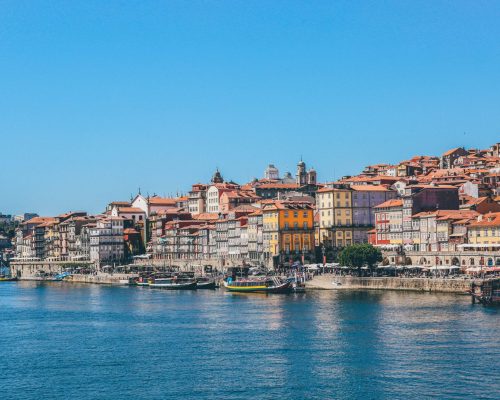 A wide shot of boats on the body of water near houses and buildings in Porto, Portugal